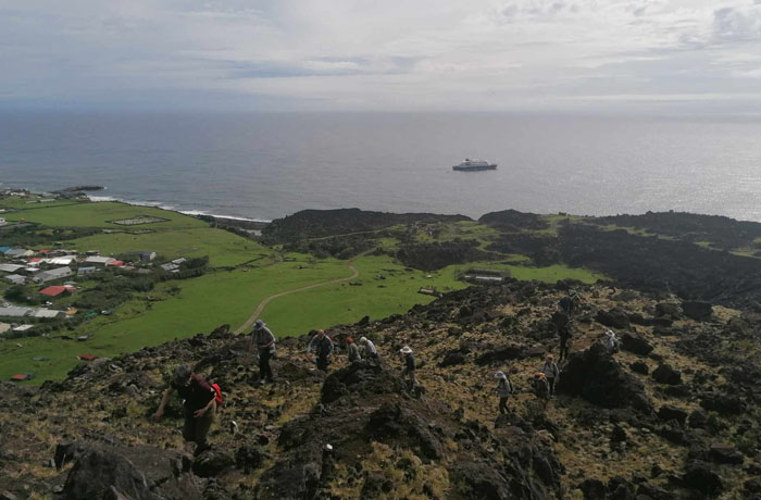 Hikers climbing the 1961 volcano with the Hondius offshore in the background