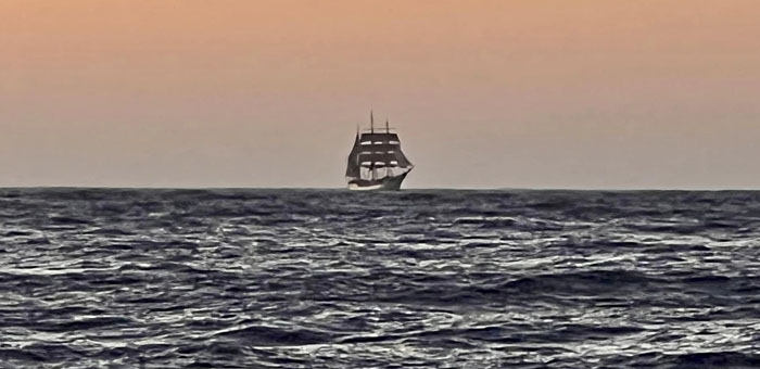 The Bark Europa in sail on the horizon and approaching the anchorage at sunset